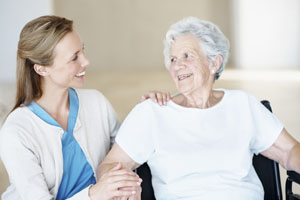 A nurse smiling at an elderly woman sitting in a wheelchair
